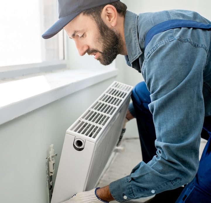 Reparaturen Handwerker installiert eine Heizkörperanlage in einem hellen Raum.