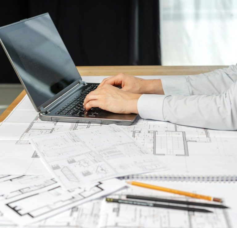 Planung & Beratung Eine Person tippt auf einem Laptop, umgeben von Bauplänen und Notizen.