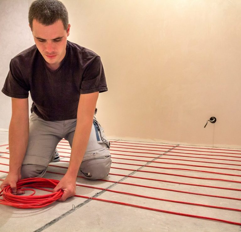 Sanierung Handwerker installiert Fußbodenheizungsleitungen auf einem Fußboden.